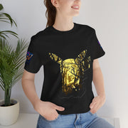 Person wearing a black t-shirt with a gold graphic design, standing indoors next to a plant.